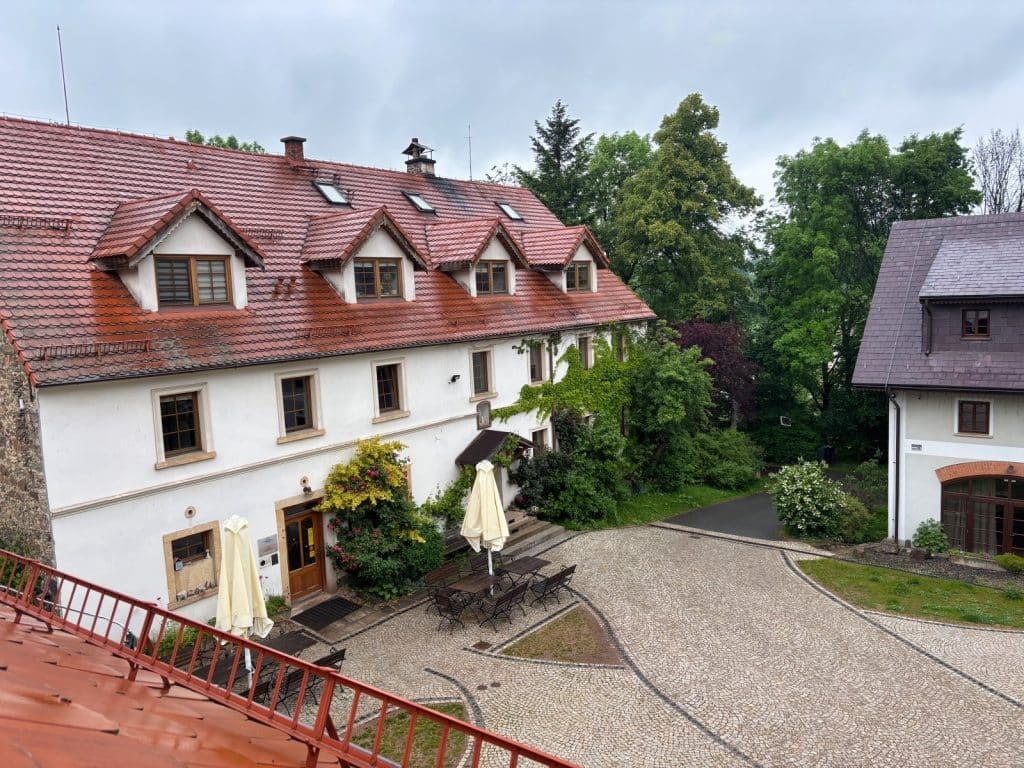 Blick von oben auf den gepflasterten Innenhof der Villa Greta in Niederschlesien mit dem weißen Haupthaus, das ein rotes Ziegeldach mit Gauben besitzt, sowie Sitzgelegenheiten unter Sonnenschirmen.