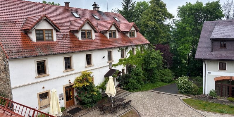 Blick von oben auf den gepflasterten Innenhof der Villa Greta in Niederschlesien mit dem weißen Haupthaus, das ein rotes Ziegeldach mit Gauben besitzt, sowie Sitzgelegenheiten unter Sonnenschirmen.