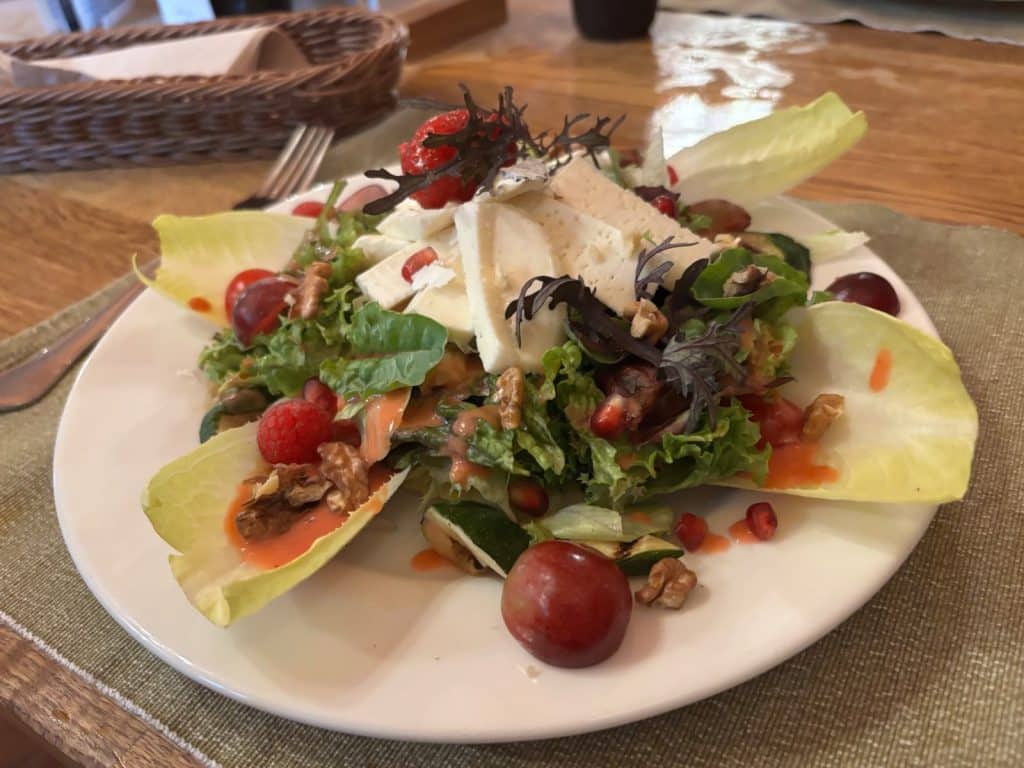 Ein bunt angerichteter Salat in der Villa Greta in Niederschlesien, serviert auf einem weißen Teller mit Chicorée-Blättern, Walnüssen, Weintrauben, Granatapfelkernen, Käsescheiben und einem fruchtigen Dressing.