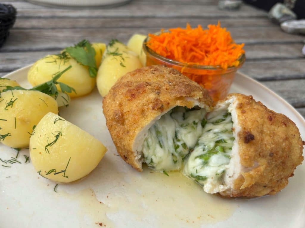 Ein Teller mit einem Tagesgericht der Villa Greta in Niederschlesien, bestehend aus einem aufgeschnittenen, mit Kräuterbutter gefüllten Kiewer Kotelett, Petersilienkartoffeln und einem Glas geraspelter Karotten.
