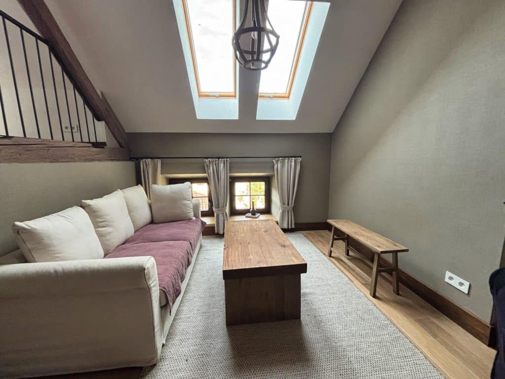 Ein gemütliches Zimmer in der Villa Greta in Niederschlesien mit einem hellen Sofa, einem rustikalen Holztisch und Dachfenstern, die viel natürliches Licht hereinlassen.