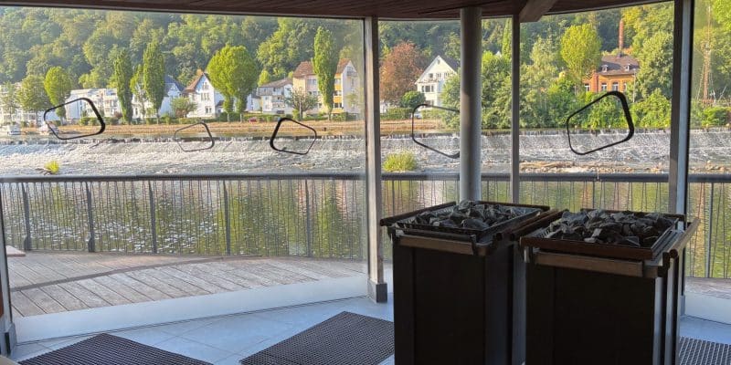 Blick aus der modernen Flusssauna der Emser Therme durch große Panoramafenster auf die Lahn, ein Wehr und die gegenüberliegenden Häuser am bewaldeten Ufer.