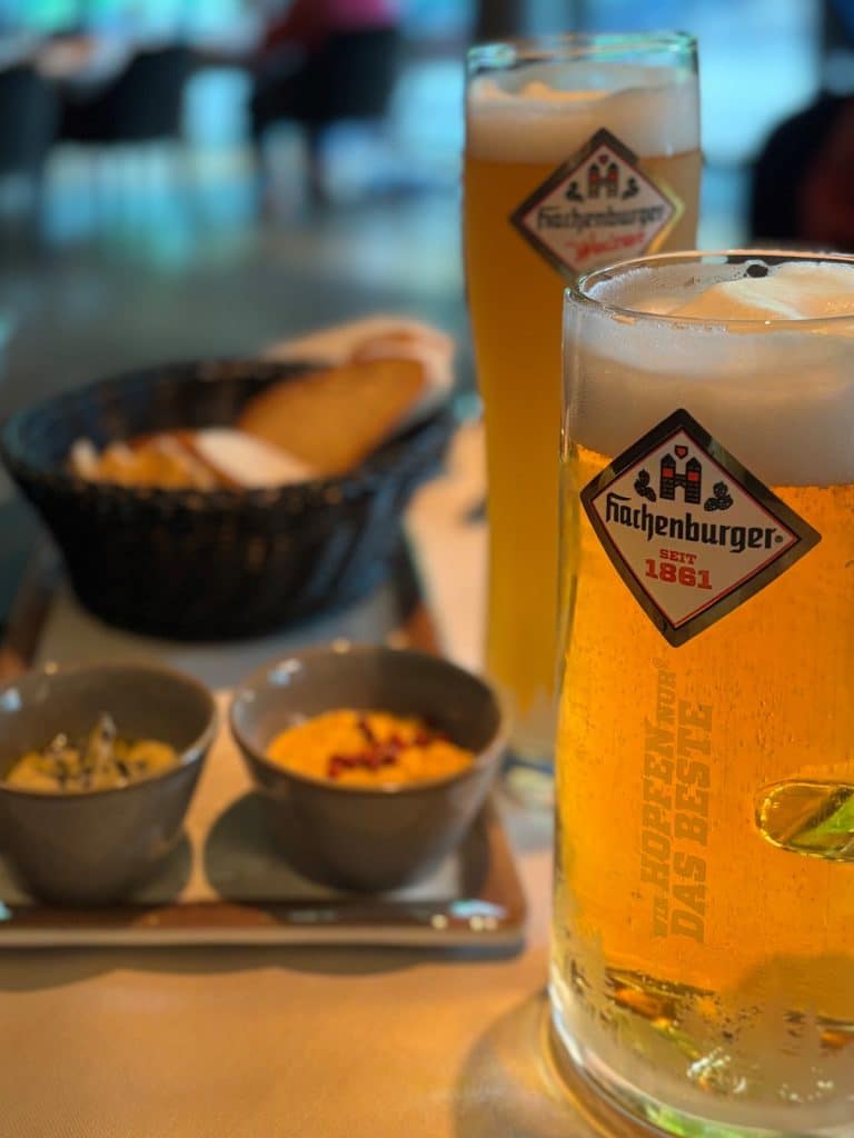 Zwei Gläser Hachenburger Bier mit Schaumkrone stehen neben kleinen Schälchen mit Dips und einem Brotkorb in einem Hotel in Bad Ems.