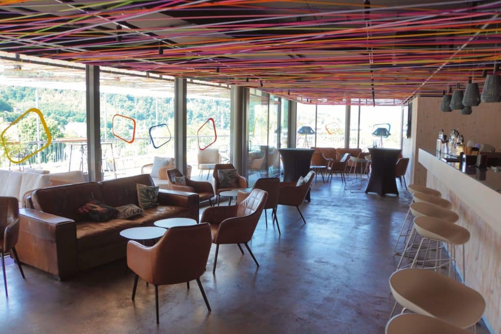 Die Skylounge des Hotels in Bad Ems präsentiert sich als moderner Innenraum mit einer bunten Fadendecke, gemütlichen Ledersofas und einer Bar mit Blick in die Natur.