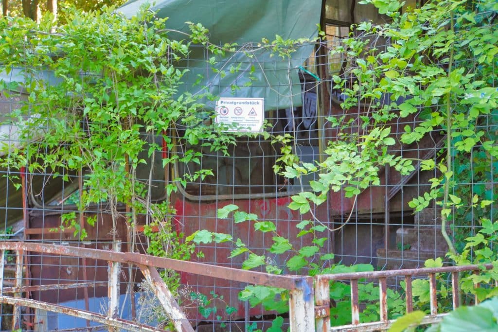 Eine überwucherte, rostrote Kabine der alten Malbergbahn in Bad Ems steht hinter einem Drahtzaun, an dem ein Schild mit der Aufschrift „Privatgrundstück“ angebracht ist.
