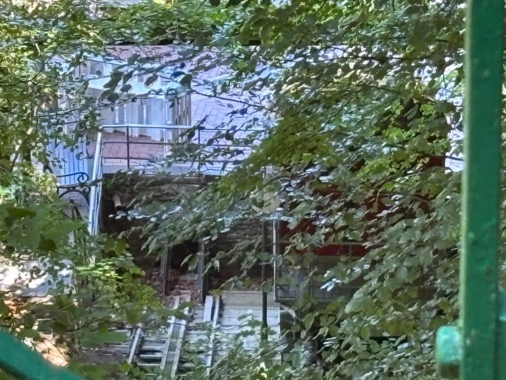 Blick durch dichtes grünes Laub auf die verfallene Bergstation der historischen Malbergbahn in Bad Ems mit sichtbaren Gleisresten und Mauerwerk.