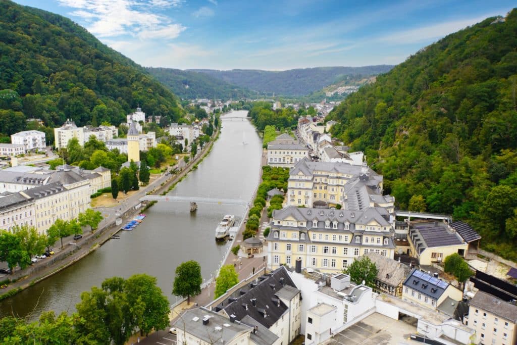 Blick von einem Aussichtspunkt auf die Kurstadt Bad Ems an der Lahn, die von bewaldeten Hügeln umgeben ist und markante historische Gebäude entlang des Flussufers zeigt.