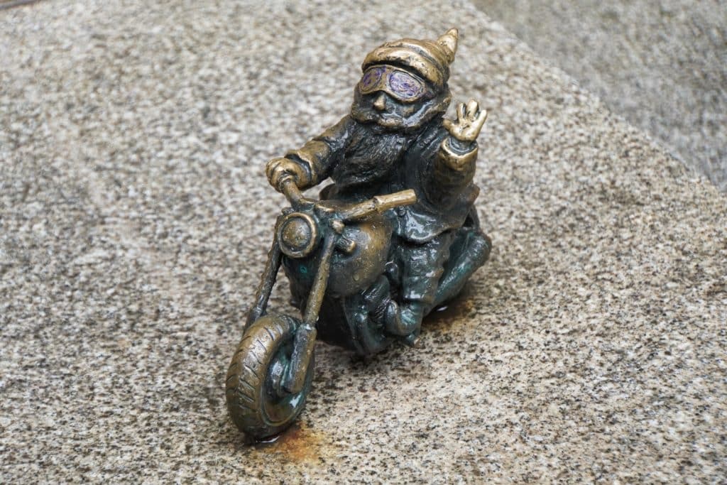 Eine kleine Bronzestatue eines Zwergs auf einem Motorrad, der mit einer Hand grüßt und eine Fliegerbrille trägt, platziert auf der Hexenbrücke in Breslau.