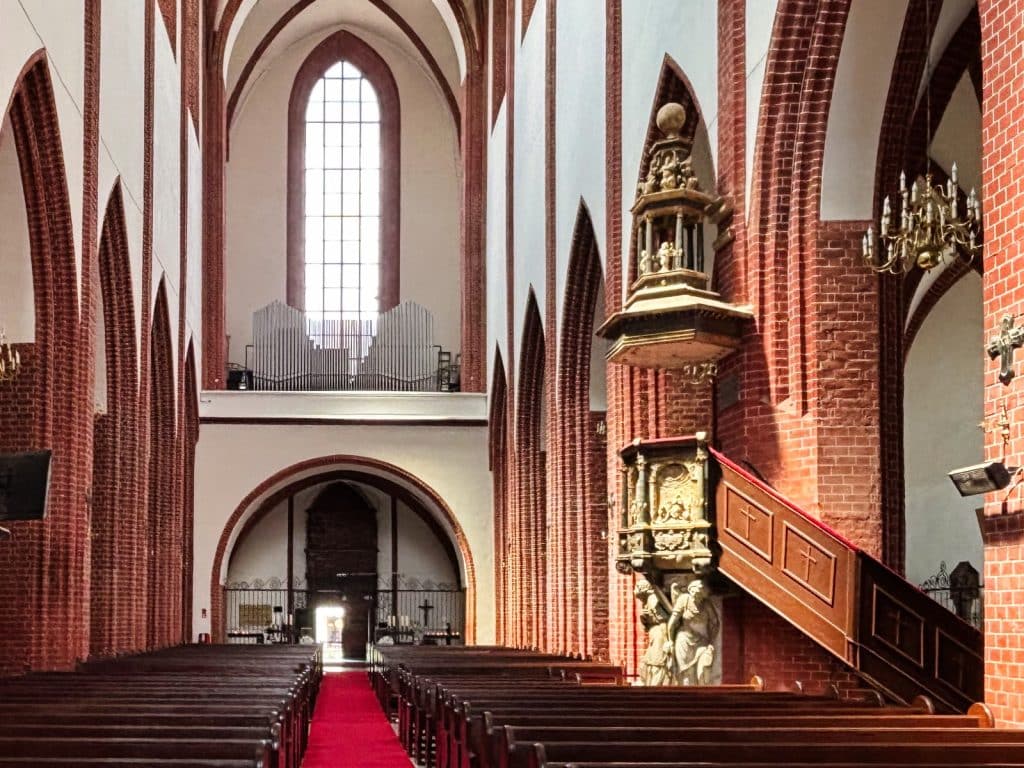 Blick in das Kirchenschiff der Maria-Magdalena-Kirche in Breslau mit einer prunkvollen, verzierten Kanzel im Vordergrund und der berühmten Hexenbrücke im Hintergrund.