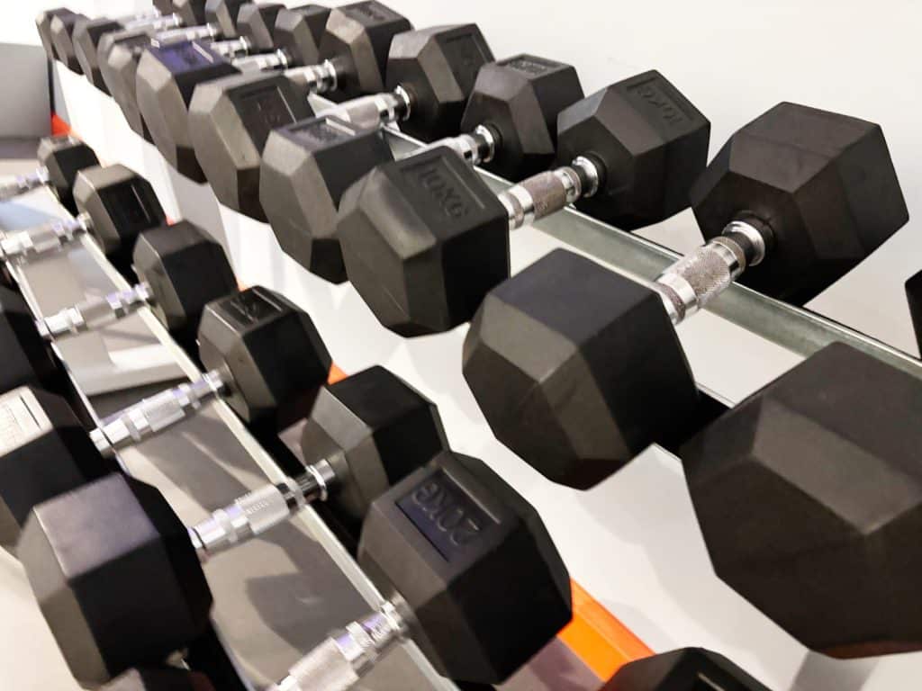 Nahaufnahme von mehreren Reihen schwarzer Hexagon-Hanteln auf silbernen Metallständern im Fitnessstudio lyf EAST FRANKFURT. Die Hanteln sind nach Gewicht sortiert, wobei die vorderste Hantel deutlich mit der Aufschrift „20 kg“ gekennzeichnet ist.