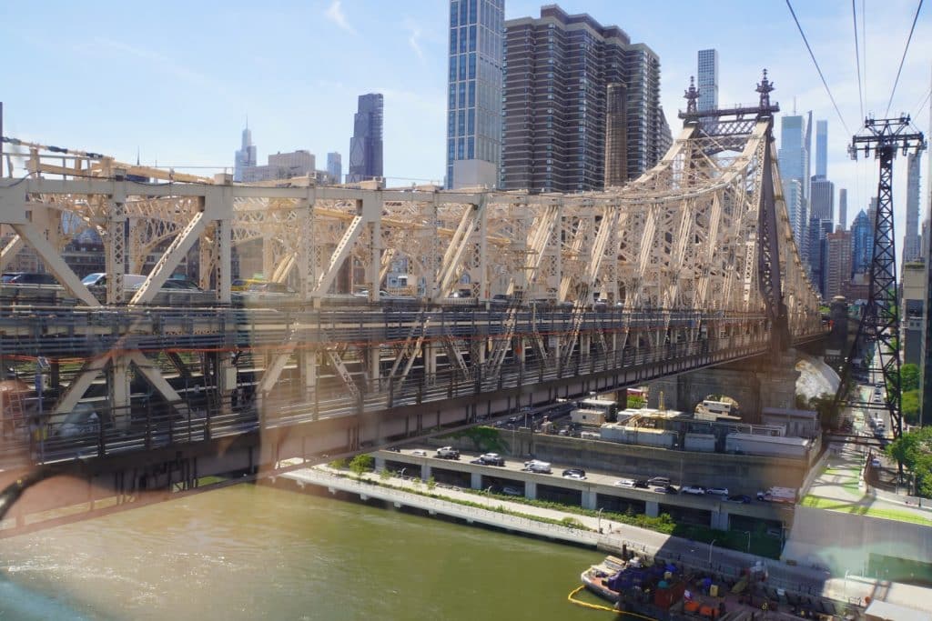 Blick aus der Roosevelt Island Seilbahn auf die stählerne Fachwerkkonstruktion der Queensboro Bridge, die über den East River führt, mit der Skyline von Manhattan im Hintergrund.