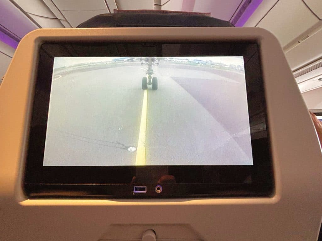 Nahaufnahme eines Bildschirms im Vordersitz eines Flugzeugs nach Curaçao, der eine Live-Übertragung der Bugradkamera während des Rollens auf der Startbahn zeigt.