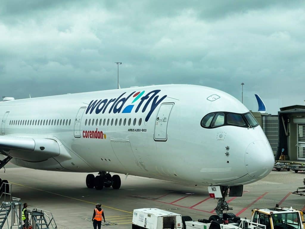 Nahaufnahme eines Airbus A350-900 von World2Fly mit Corendon-Logo auf dem Rollfeld, bereit für den Flug nach Curacao. Das Flugzeug wird von Bodenpersonal und Servicefahrzeugen unter einem bewölkten Himmel abgefertigt.
