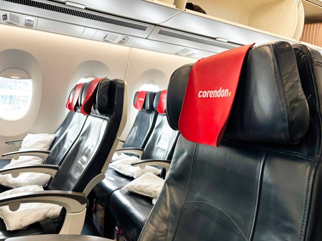 Innenansicht eines Flugzeugs von Corendon Airlines auf dem Weg nach Curaçao mit leeren, dunkelblauen Ledersitzen, die rote Kopfstützenbezüge und weiße Kissen aufweisen.