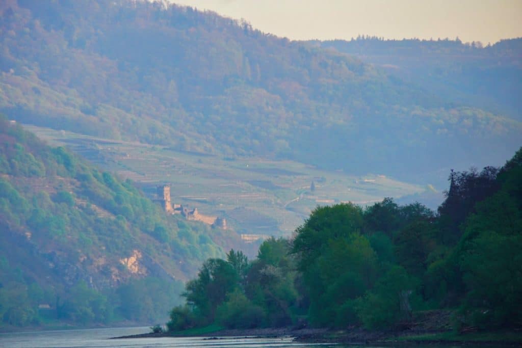 Blick vom Wasser auf eine bewaldete Hügellandschaft an der Donau bei Passau, an deren Hängen eine historische Burgruine über dem Fluss thront.