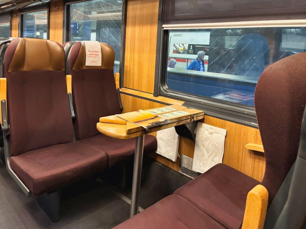 Innenansicht eines Snälltåget-Reisezug mit vier weinroten Sitzen, die um einen kleinen Holztisch an einem Fenster angeordnet sind.