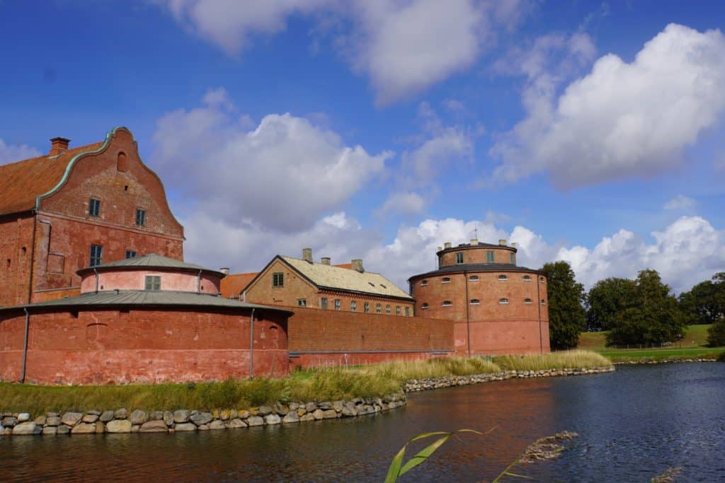 Die historische Zitadelle von Landskrona mit ihren markanten roten Backsteingebäuden und Rundtürmen spiegelt sich an einem sonnigen Tag im Wasser des umgebenden Festungsgrabens.